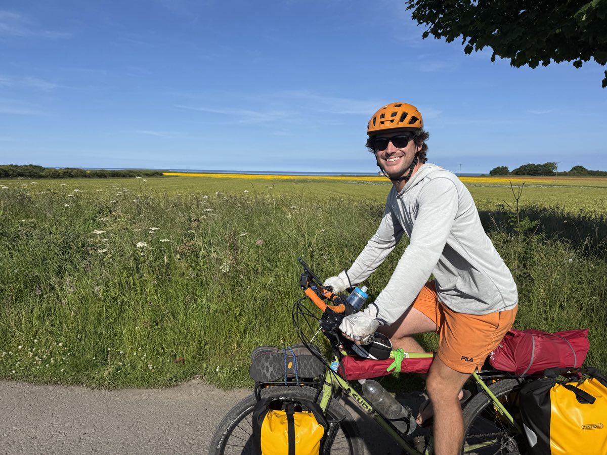 Riding a loaded touring bike along a coastal lane past a field of yellow rapeseed, on the Europe bike tour
